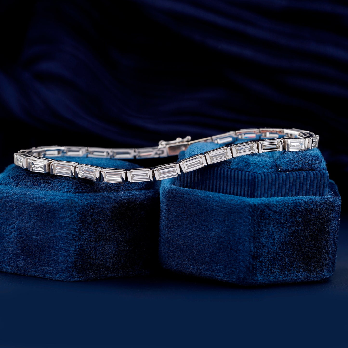 Bracelet with white metal links, rectangular step-cut stones in tennis bracelet design, displayed across blue velvet ring boxes, angled view
