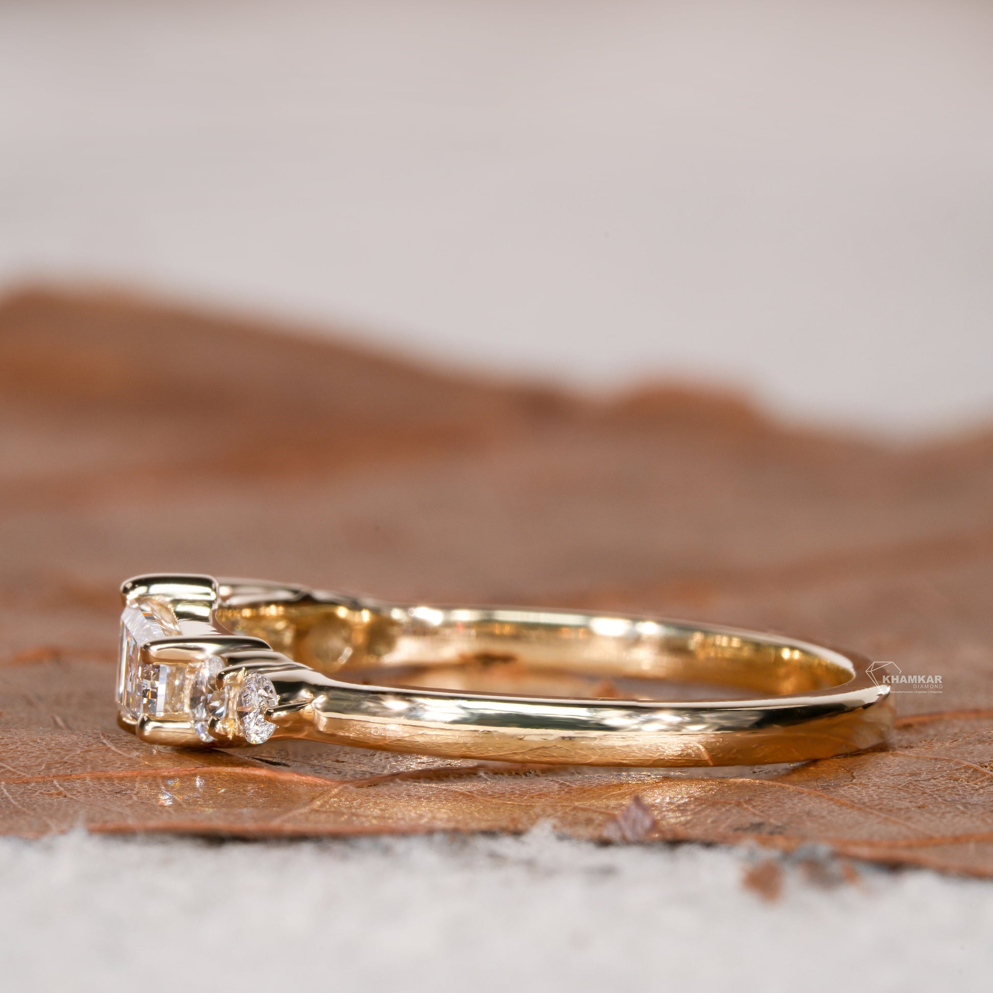 Engagement ring with yellow gold band, horizontal baguette-cut clear center gemstone and round side stones, side profile view
