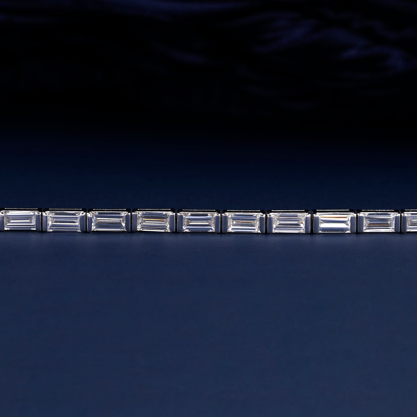 Bracelet with white metal links, rectangular step-cut stones in tennis bracelet design, close-up front detail view on a dark background
