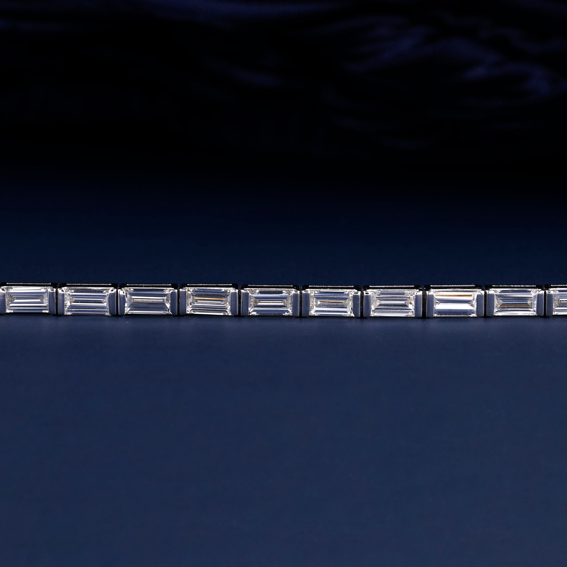 Bracelet with white metal links, rectangular step-cut stones in tennis bracelet design, close-up front detail view on a dark background
