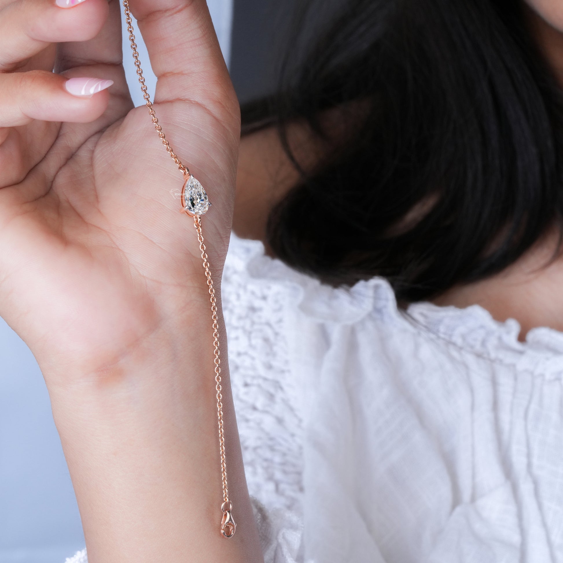 Bracelet with pear-shaped clear stone on yellow metal chain, held in hand, close-up lifestyle view, delicate chain bracelet jewelry
