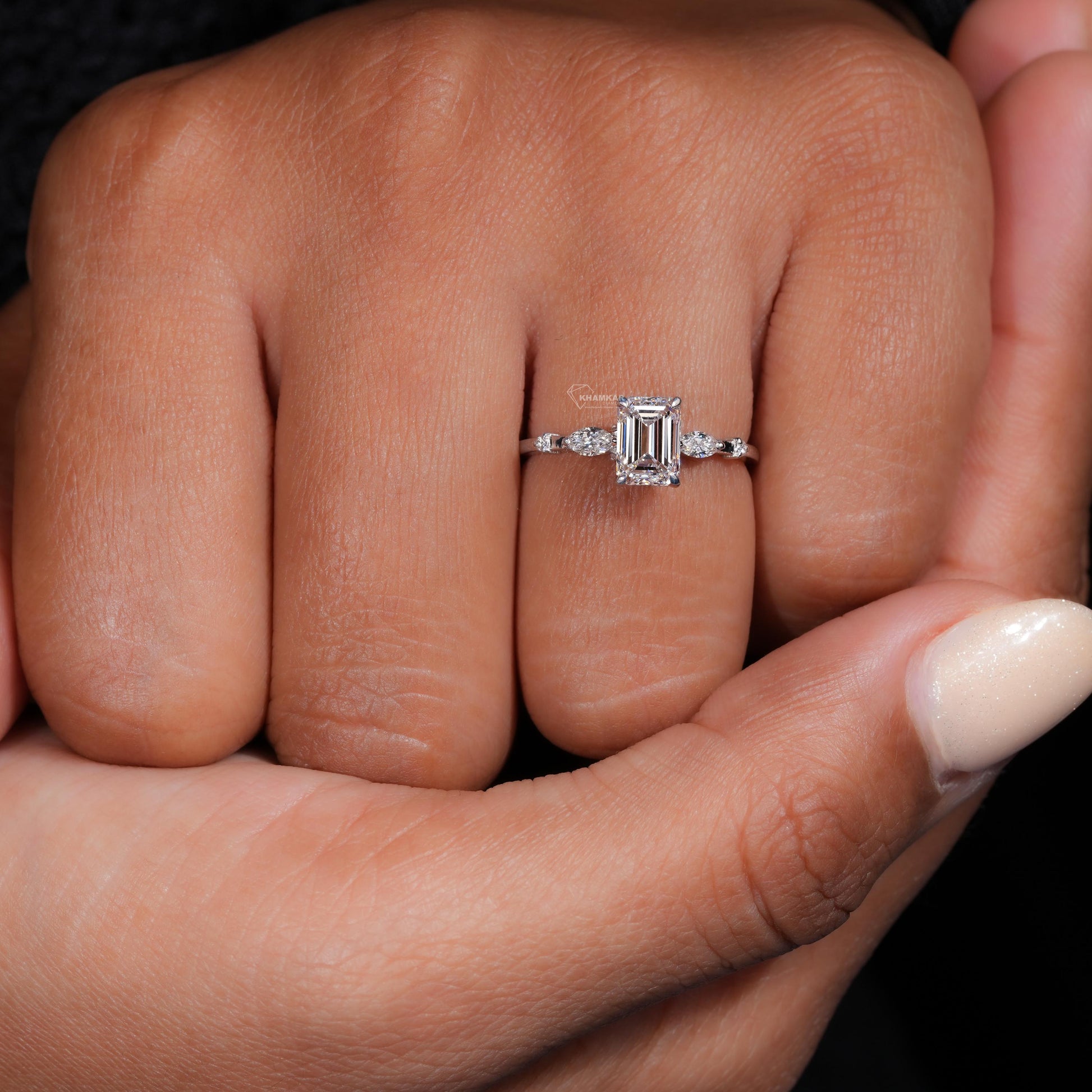 Engagement ring with white metal band, emerald-cut clear center stone, marquise side stones and round accents, worn on finger front view
