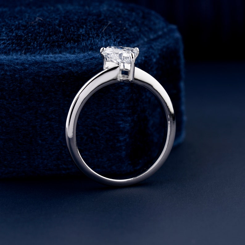 Solitaire ring with clear geometric center stone in raised prong setting and polished white metal band, rear view
