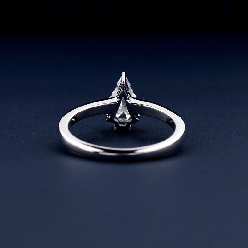 Engagement ring with polished white metal band and raised clear center stone in prong setting, rear view on dark blue surface
