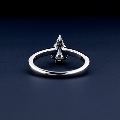 Engagement ring with polished white metal band and raised clear center stone in prong setting, rear view on dark blue surface
