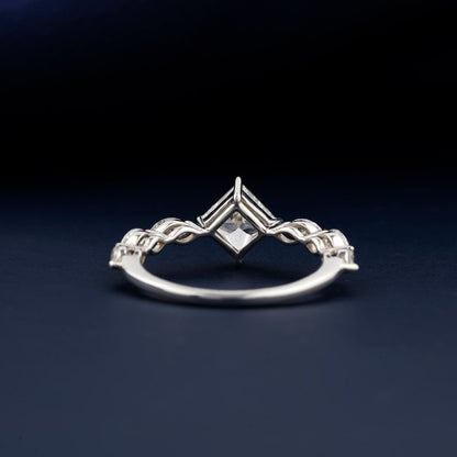 Engagement ring with white metal twisted band, princess-cut center stone, marquise side stones, rear view showing open gallery setting on dark blue surface
