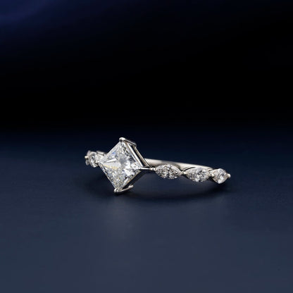 Engagement ring with white metal twisted band, princess-cut center stone, marquise side stones, side profile on dark blue surface
