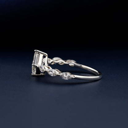 Engagement ring with white metal twisted band, princess-cut center stone, marquise side stones, side profile showing basket setting on dark blue surface
