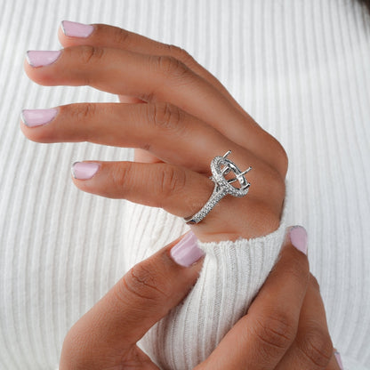 Engagement ring with white metal oval halo setting, pavé band, open four-prong center setting, side view worn on finger
