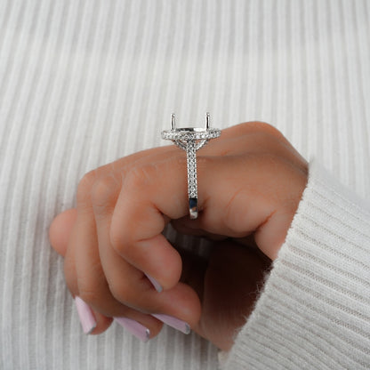 Engagement ring with white metal oval halo setting, pavé band, open four-prong center setting, side profile worn on finger
