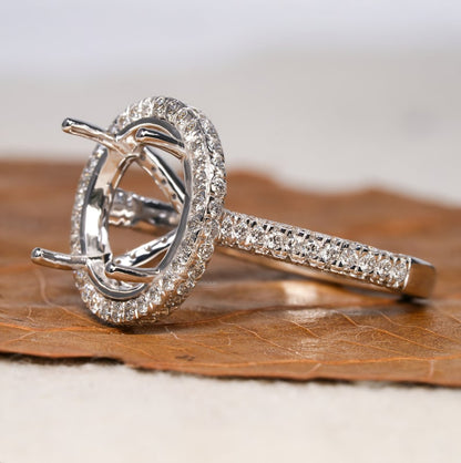 Engagement ring with white metal band, oval halo setting, pavé band, open four-prong center setting, angled side view
