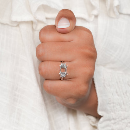 Engagement ring with white metal band, rectangular open center setting, tapered side stones, worn on hand, front view
