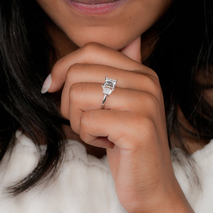 Engagement ring with white metal band, rectangular open center setting, tapered side stones, worn on hand, angled side view
