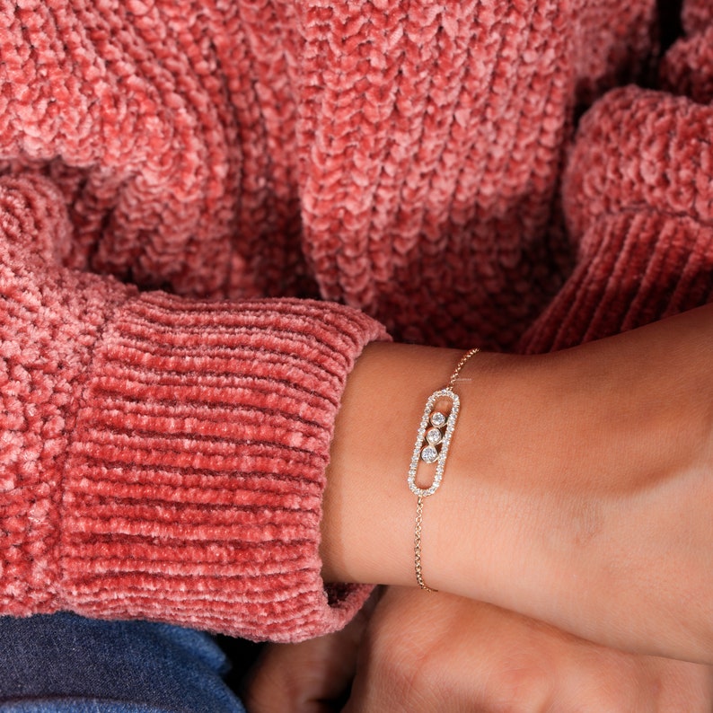 Bracelet with yellow metal chain, oval open-link centerpiece, pavé-set border and three round stones, worn on wrist, top view
