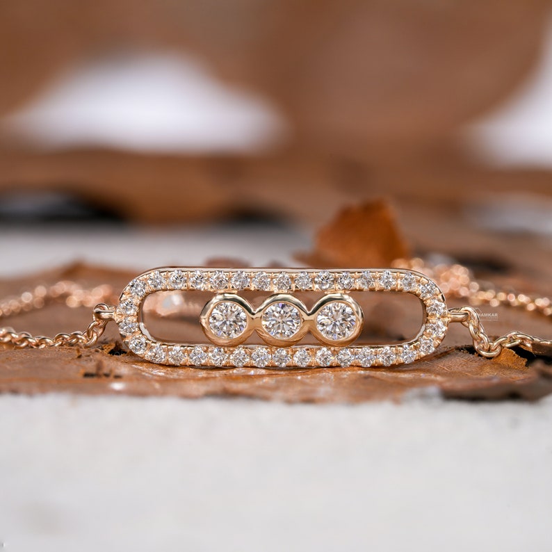 Bracelet with yellow metal chain, oval open-link centerpiece, pavé-set border and three round stones, close-up front view on wooden surface
