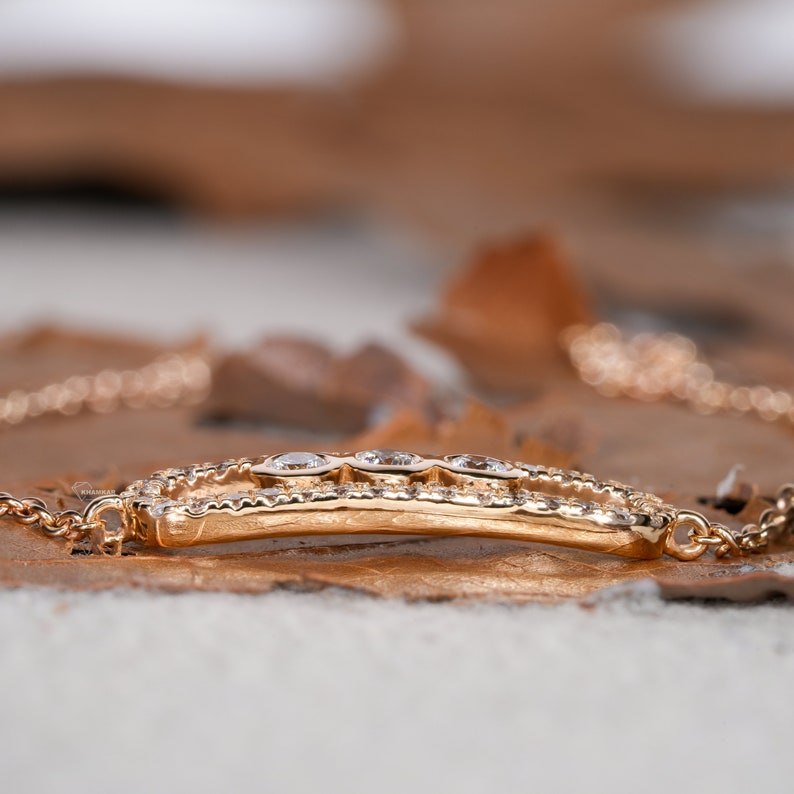 Bracelet with yellow metal chain, oval open-link centerpiece, pavé-set border and three round stones, side profile view on wooden surface
