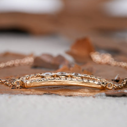 Bracelet with yellow metal chain, oval open-link centerpiece, pavé-set border and three round stones, side profile view on wooden surface
