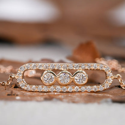 Bracelet with yellow metal chain, oval pavé-set link centerpiece and three round bezel-set stones, front view on wooden surface
