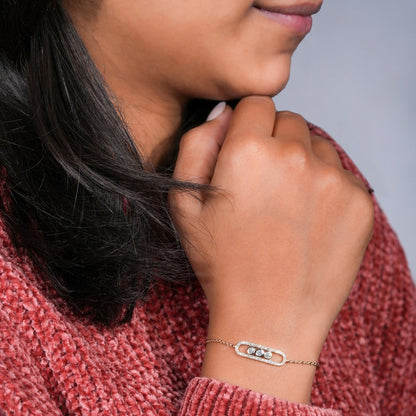 Bracelet with yellow metal chain, oval pavé-set link centerpiece and three round bezel-set stones, worn on wrist, angled view
