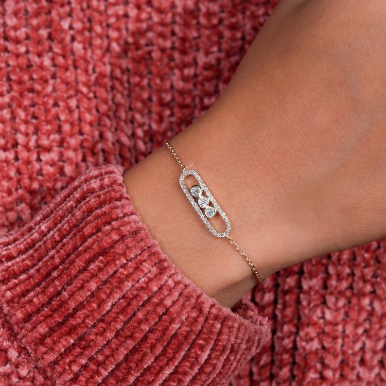 Bracelet with yellow metal chain, oval pavé-set link centerpiece and three round bezel-set stones, worn on wrist, close-up angled view
