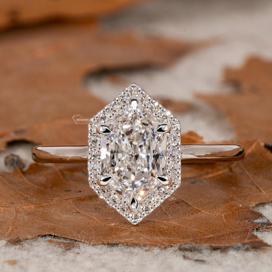 Engagement ring with silver-tone band, elongated hexagon halo setting, clear elongated faceted center stone, front view on a brown leaf surface
