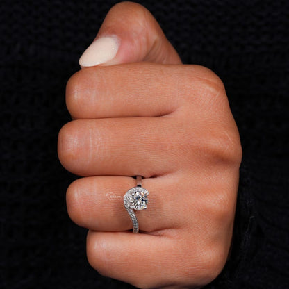 Engagement ring with round center stone, white metal swirl halo design, pavé accent band, worn on hand, front view

