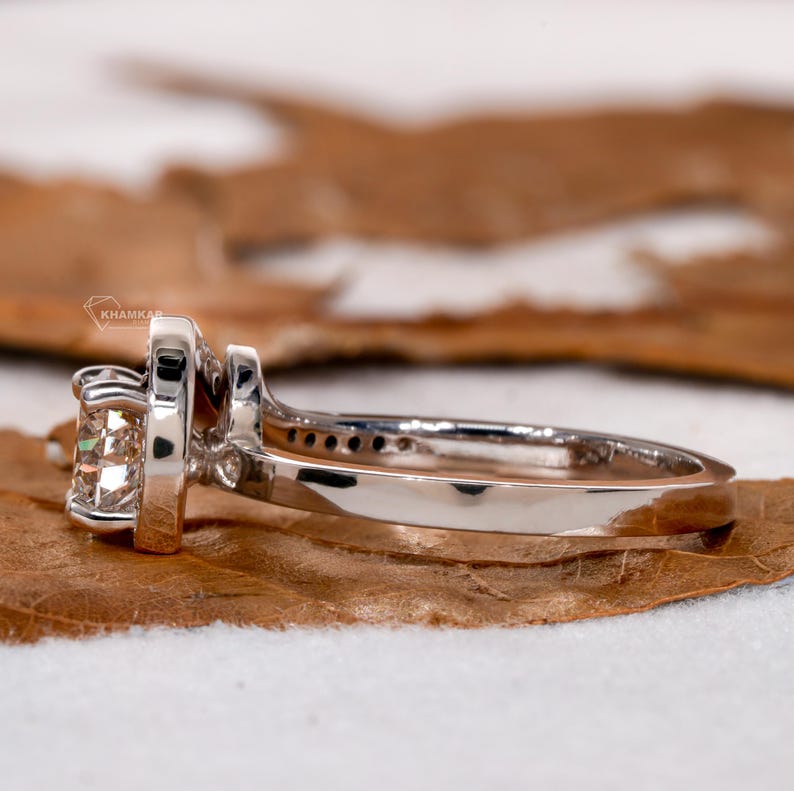 Engagement ring with round center stone, white metal swirl setting, side profile view
