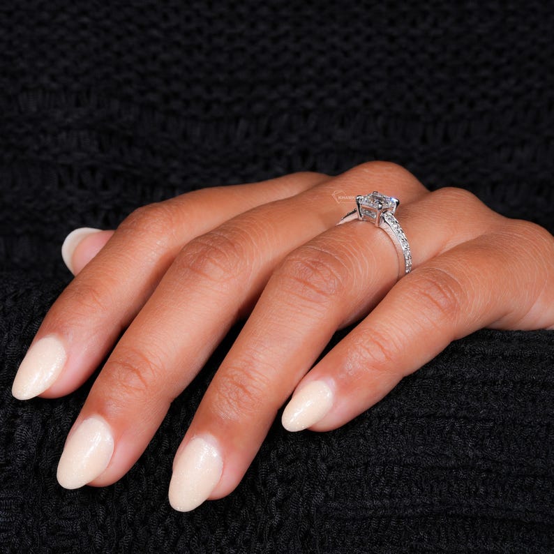 Engagement ring with white metal band, square center stone, pavé shoulders and raised four-prong setting, worn on hand, side angle
