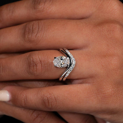 Engagement ring set with oval solitaire diamond and curved pavé wedding band worn on a finger, top view on hand