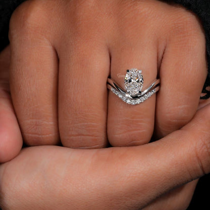 Engagement ring set with oval solitaire diamond and curved pavé wedding band worn on a finger, close-up hand view