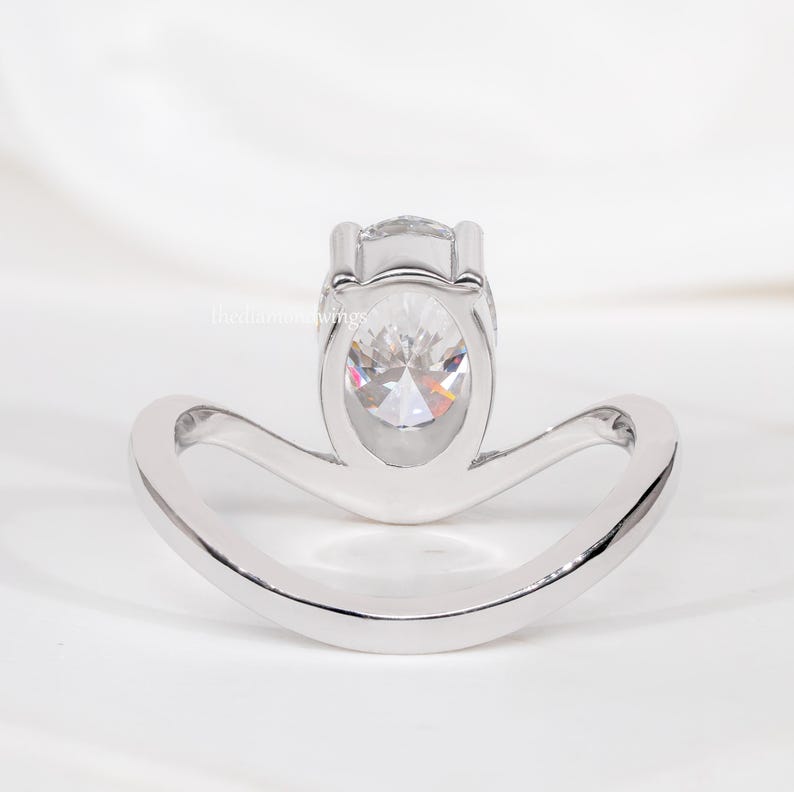 Engagement ring with oval cut clear center stone, silver tone curved solitaire band, open gallery setting, rear view