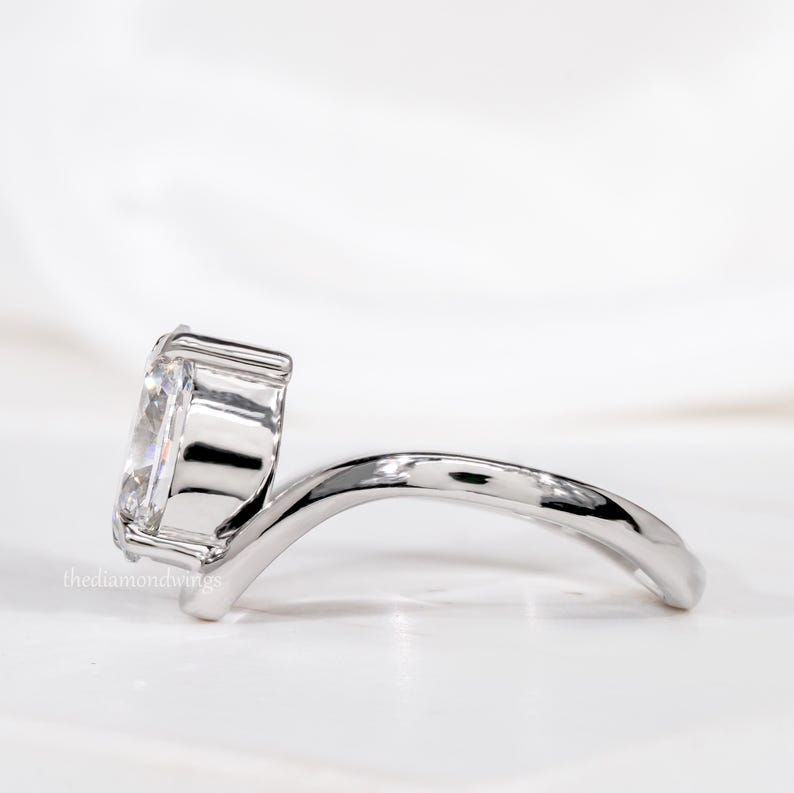Engagement ring with oval cut clear center stone, silver tone curved solitaire band, side profile view