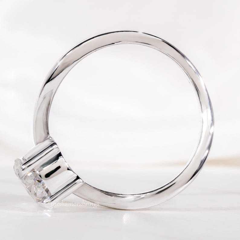 Engagement ring with oval cut clear center stone, silver tone curved solitaire band, side profile showing full band design