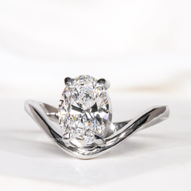 Engagement ring with oval cut clear center stone, silver tone curved solitaire band, four-prong setting, angled front view