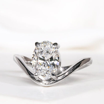 Engagement ring with oval cut clear center stone, silver tone curved solitaire band, four-prong setting, angled front view