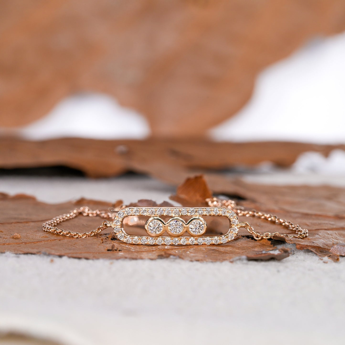 Bracelet with yellow metal chain, oval open-link centerpiece, pavé border and three round stones, front view on wooden surface
