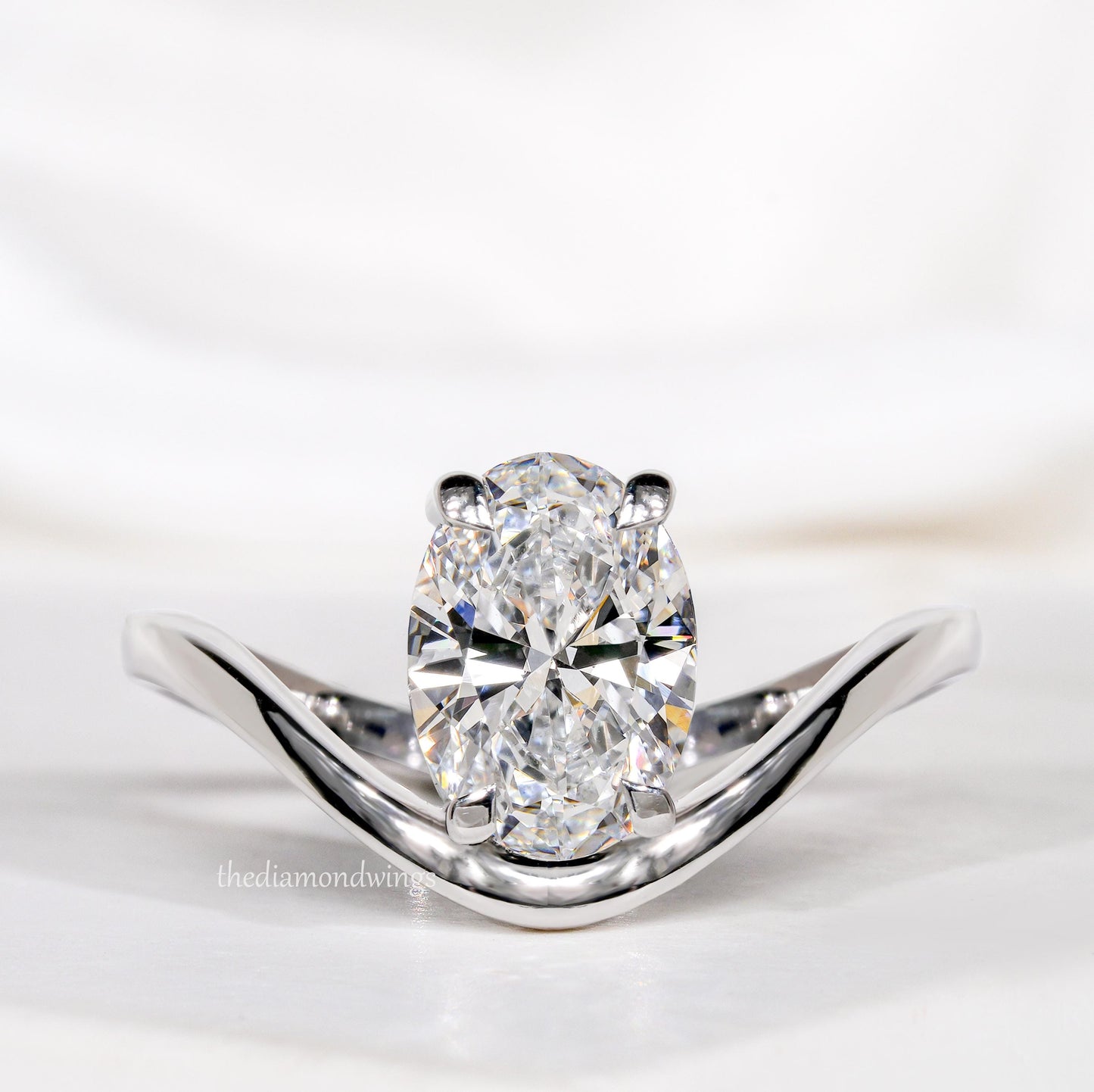 Engagement ring with oval cut clear center stone, silver tone band with four-prong setting, front close-up view