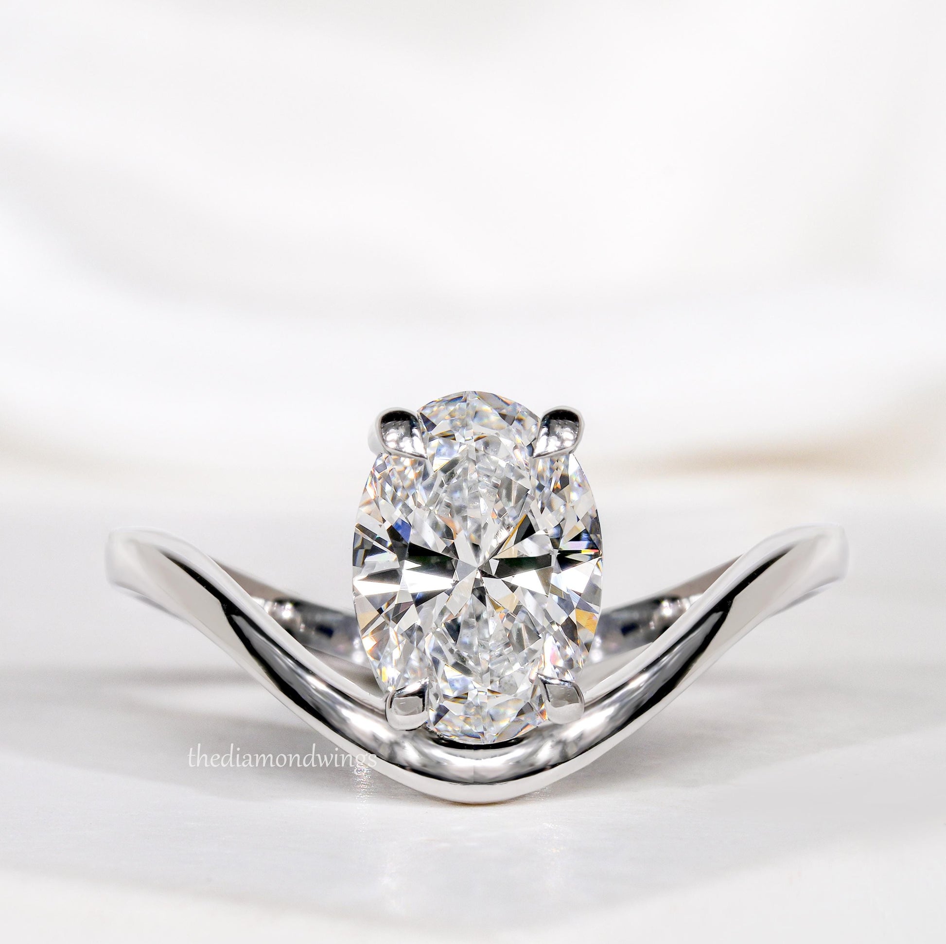 Engagement ring with oval cut clear center stone, silver tone band with four-prong setting, front close-up view