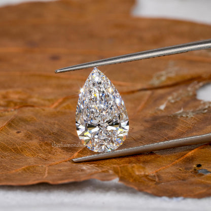 Loose pear-cut diamond, clear faceted gemstone held with tweezers on a leaf surface, front view with pointed tip and rounded base
