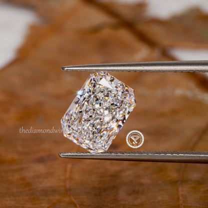 Loose radiant-cut diamond, clear faceted gemstone held with tweezers, angled top view with cropped certification seal and watermark visible
