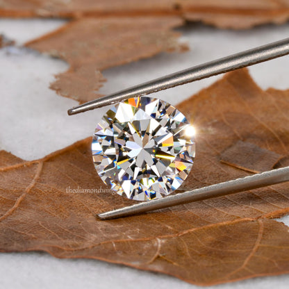 Loose round brilliant-cut diamond held with tweezers, faceted clear stone, front view
