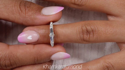 Engagement ring with white metal band, vertical baguette-cut clear center gemstone and round side stones, worn on finger, front view
