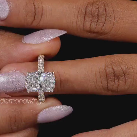 Engagement ring with two cushion-cut clear gemstones, polished yellow metal pavé band, four-prong setting, worn on finger, front view
