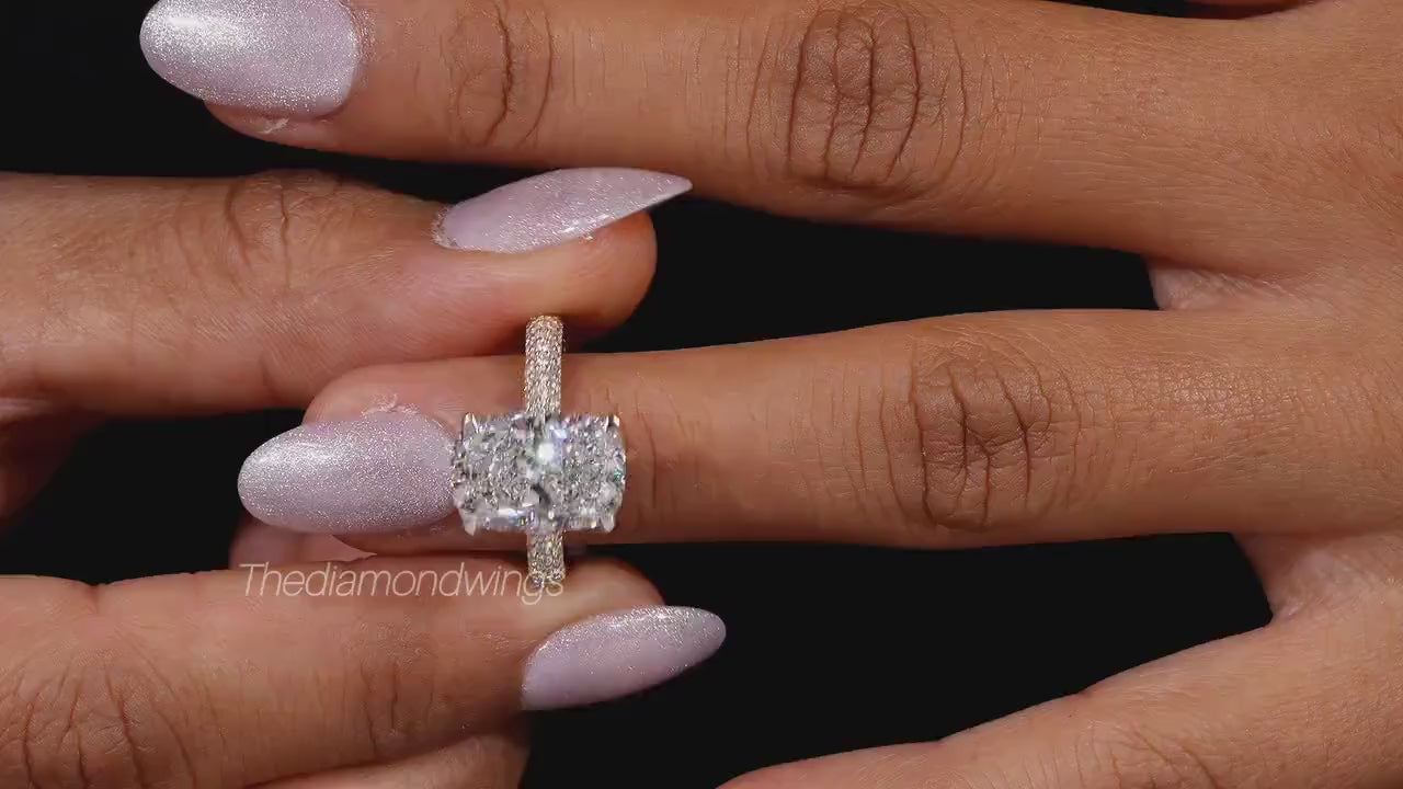 Engagement ring with two cushion-cut clear gemstones, polished yellow metal pavé band, four-prong setting, worn on finger, front view

