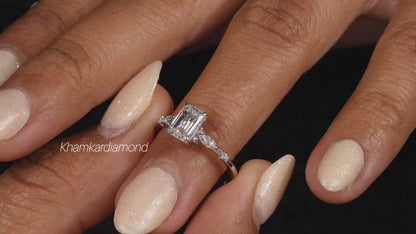 Engagement ring with white metal band, emerald-cut clear center stone, marquise side stones, worn on finger at angled view
