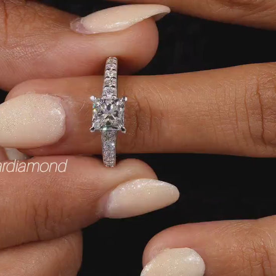 Engagement ring with white metal pavé band, square center stone in four-prong setting, worn on finger, front view
