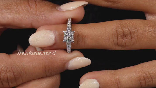Engagement ring with white metal pavé band, square center stone in four-prong setting, worn on finger, front view

