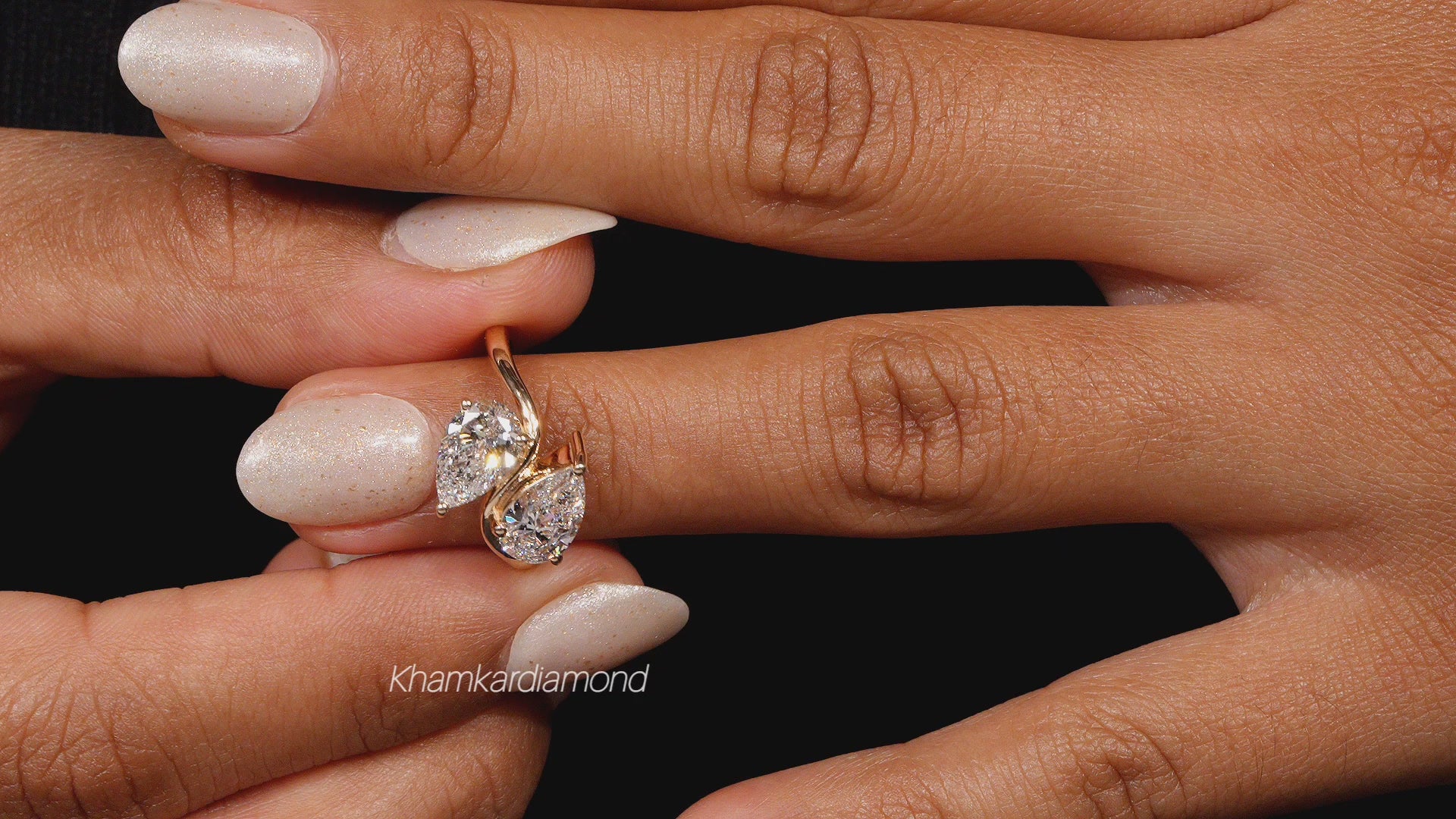 Engagement ring with yellow metal bypass band, two pear-shaped clear gemstones, worn on finger, close-up front view
