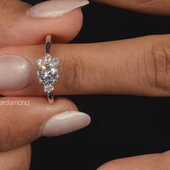 Engagement ring with white metal, oval center stone, round accent diamonds, cluster setting, worn on finger, front view
