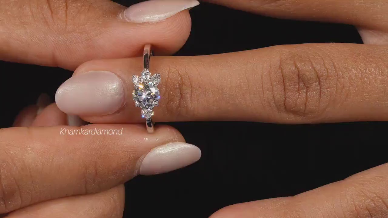 Engagement ring with white metal, oval center stone, round accent diamonds, cluster setting, worn on finger, front view
